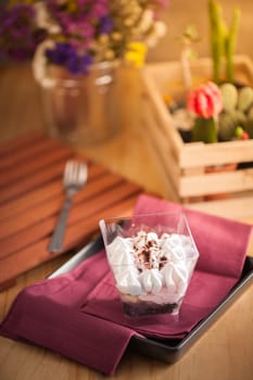 Banoffee pie in plastic cup on red napkin in black dish on wood table with afternoon scene