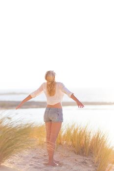 Relaxed woman enjoying freedom and life an a beautiful sandy beach.  Young lady feeling free, relaxed and happy. Concept of happiness, enjoyment and well being.  Enjoying Sun on Vacations. Copyspace.