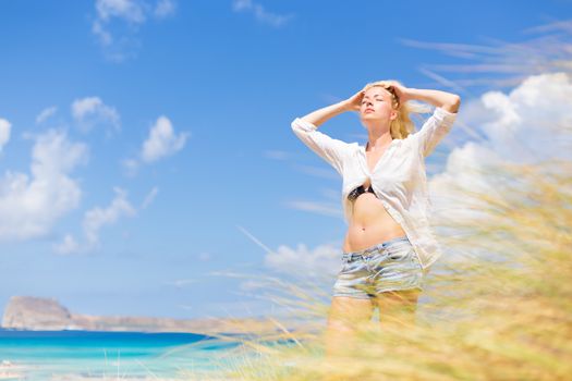 Relaxed woman enjoying freedom and life an a beautiful sandy beach.  Young lady feeling free, relaxed and happy. Concept of freedom, happiness, enjoyment and well being.  Enjoying Sun on Vacations.