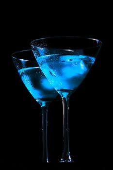 view from below of glasses of fresh blue cocktail with ice on blue tint light and black background