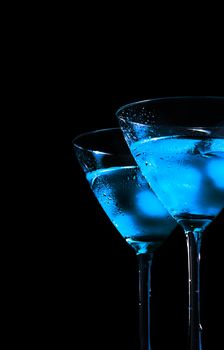 glasses of fresh blue cocktail with ice on blue tint light and black background with space for text