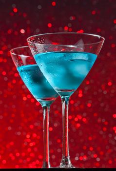 view from below of glasses of fresh blue cocktail with ice on red tint light bokeh background on bar table