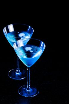 two glasses of fresh blue cocktail with ice on blue tint light and black background on wood table with space for text