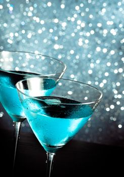 a pair of glasses of fresh blue cocktail with ice on blue tint light bokeh background on bar table