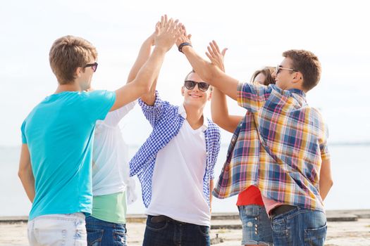 friendship, leisure, summer, gesture and people concept - group of smiling friends making high five outdoors