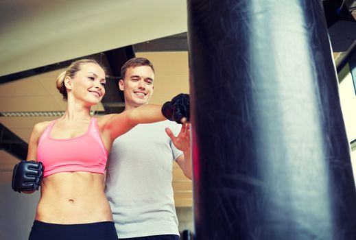 sport, fitness, lifestyle and people concept - smiling woman with personal trainer boxing punching bag in gym