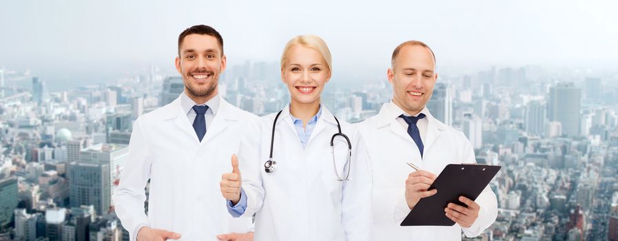 healthcare, people, gesture and medicine concept - group of doctors with stethoscope and clipboard showing thumbs up over city background