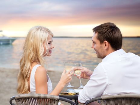 summer holidays, people, romance, travel and dating concept - couple drinking wine in cafe on sunset beach