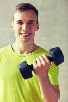 sport, fitness, lifestyle and people concept - smiling man with dumbbell flexing biceps in gym