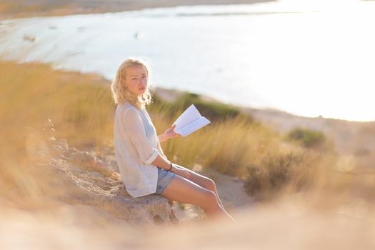 Relaxed woman enjoys reading on beautiful sandy beach.  Young lady with book in her hand. Concept of happiness, enjoyment and well being.  Enjoying Sun on Vacations. 