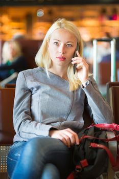 Casual blond young woman calling by cell phone while waiting to board a plane at the departure gates. Wireless network hotspot enabling people to access internet conection. Public transport.