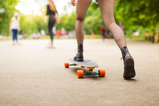 Teenage girl wearing black boots and stockings practicing long board riding outdoors in skateboarding park. Active urban life. Urban subculture. Motion blured. Focus on the floor for copy space.