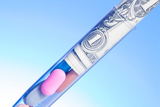 colorful pills and dollars in test tube, cost of medical health care on light blue background