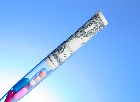 colorful pills and dollars in test tube, cost of medical health care on light blue background