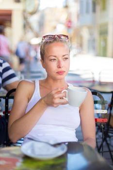 Calm casual blond lady enjoying cup of coffee outdoor in typical italian  street coffee house on warm summer day.