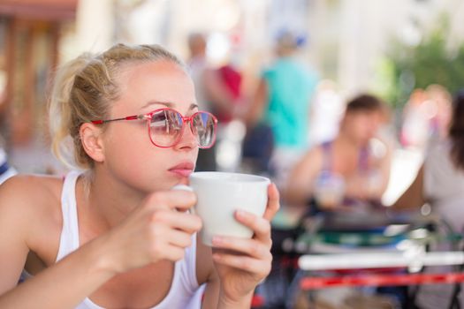 Calm casual blond lady enjoying cup of coffee outdoor in typical italian  street coffee house on warm summer day.