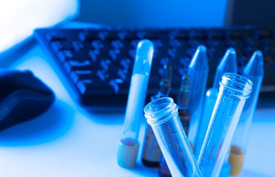 test tubes in laboratory on table near computer keyboard and mouse on blue light tint background