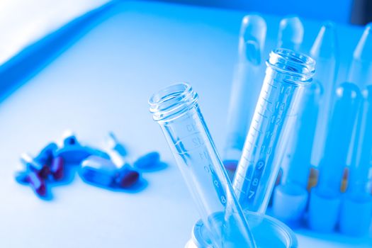 detail of test tubes in laboratory near pills on blue light tint background