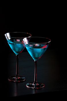 glasses of fresh blue cocktail with ice on red tint light and black background on bar table with space for text