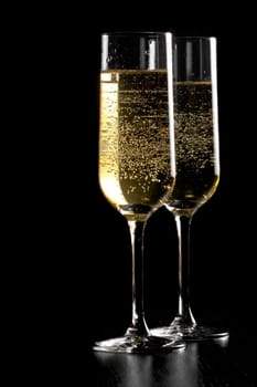 a pair of flutes of champagne with golden bubbles on black wood background and space for text