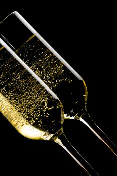 detail of a pair of tilted flutes of champagne with golden bubbles on black background