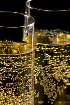 a pair of flutes of champagne tilted with golden bubbles on black background and space for text