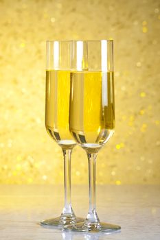 a pair of flutes of champagne on golden bokeh background on table