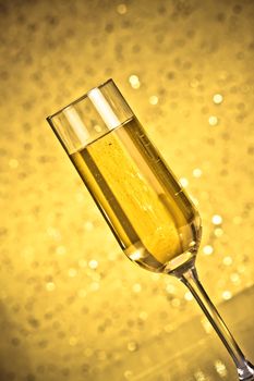 tilted flute of golden champagne on dark golden bokeh background on table