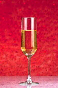 one flute of golden champagne on red bokeh background