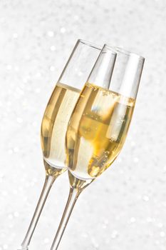 a pair of flutes of golden champagne on silver bokeh background