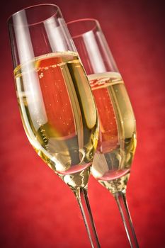 a pair of flutes of golden champagne on red background