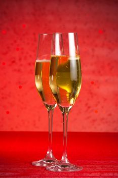 a pair of flutes of champagne on red bokeh background and red table