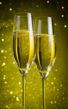 two champagne flutes with golden bubbles on yellow light bokeh background