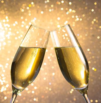 pair of a champagne flutes with golden bubbles make cheers on light bokeh background