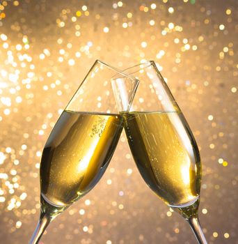 champagne flutes with golden bubbles make cheers on light bokeh background