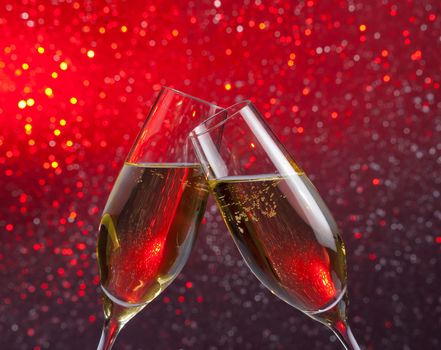 pair of a champagne flutes with gold bubbles make cheers on red and violet light bokeh background