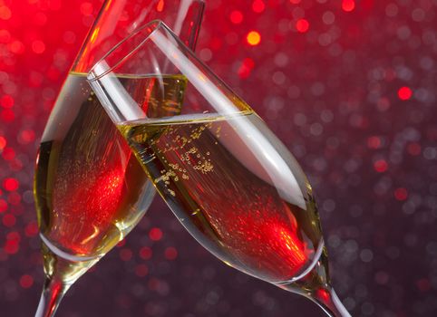 pair of champagne flutes with gold bubbles make cheers on red light bokeh background