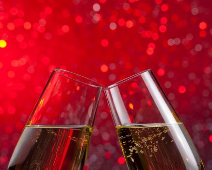 pair of champagne flutes with gold bubbles make cheers on red light bokeh background with space for text