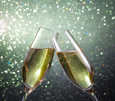 champagne flutes with gold bubbles make cheers on green light bokeh background