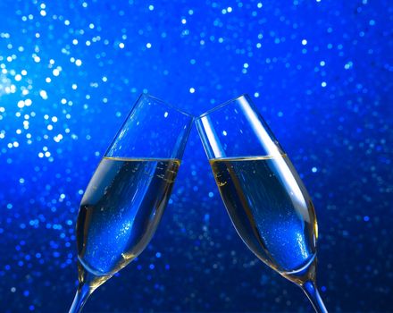 a pair of champagne flutes make cheers on blue light bokeh background with space for text