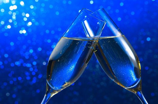 pair of a champagne flutes make cheers on blue light bokeh background with space for text