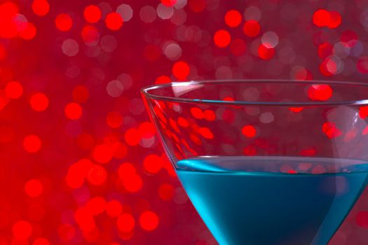 one glass blue cocktail on red tint light bokeh background
