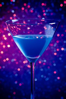 one glass blue cocktail on blue and violet tint light bokeh background