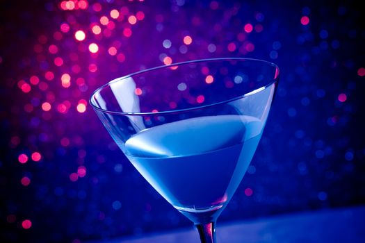 glass blue cocktail on blue and violet tint light bokeh background on table
