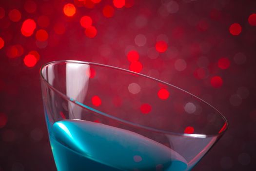 detail of one glass blue cocktail on red tint light bokeh background