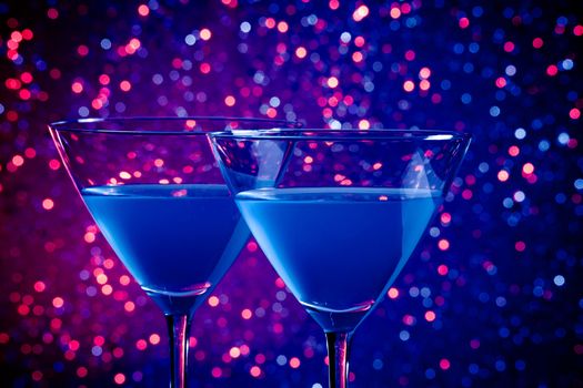 two glasses of blue cocktail on blue and violet tint light bokeh background