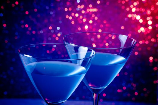 detail of a pair of glasses of blue cocktail on blue and violet tint light bokeh background