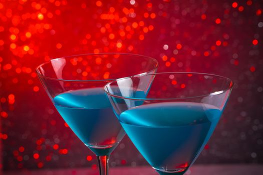 detail of a pair of glasses of blue cocktail on red tint light bokeh background