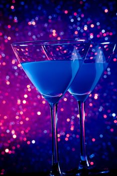 a pair of glasses of blue cocktail on blue and violet tint light bokeh background