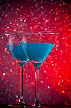 a pair of glasses of blue cocktail on red tint light bokeh background